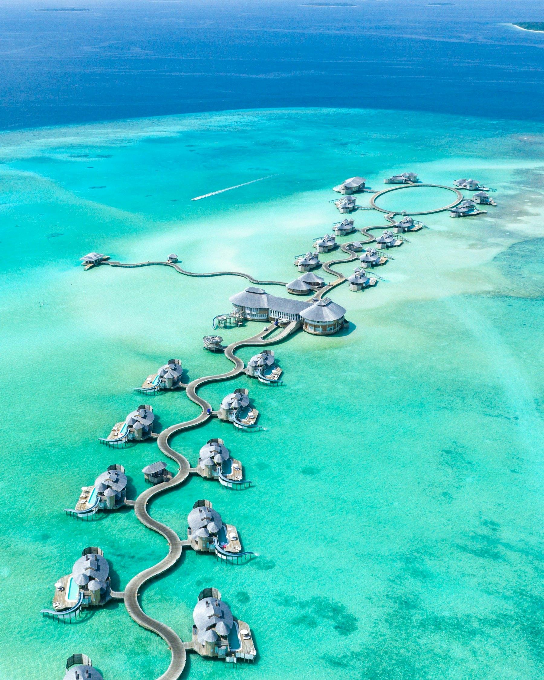 Aerial view of overwater villas curving across a turquoise Maldivian lagoon